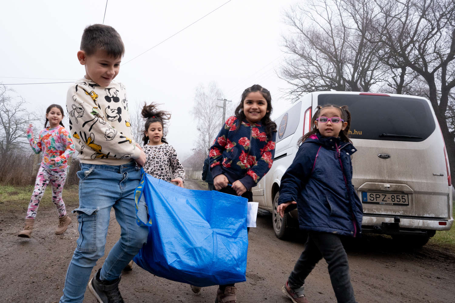 Children running towards the minibus with gift packages on a village road