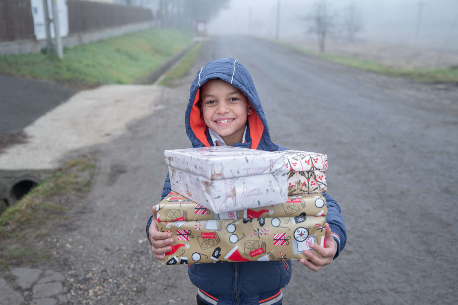 Smiling boy holding Christmas gift packages on a foggy road