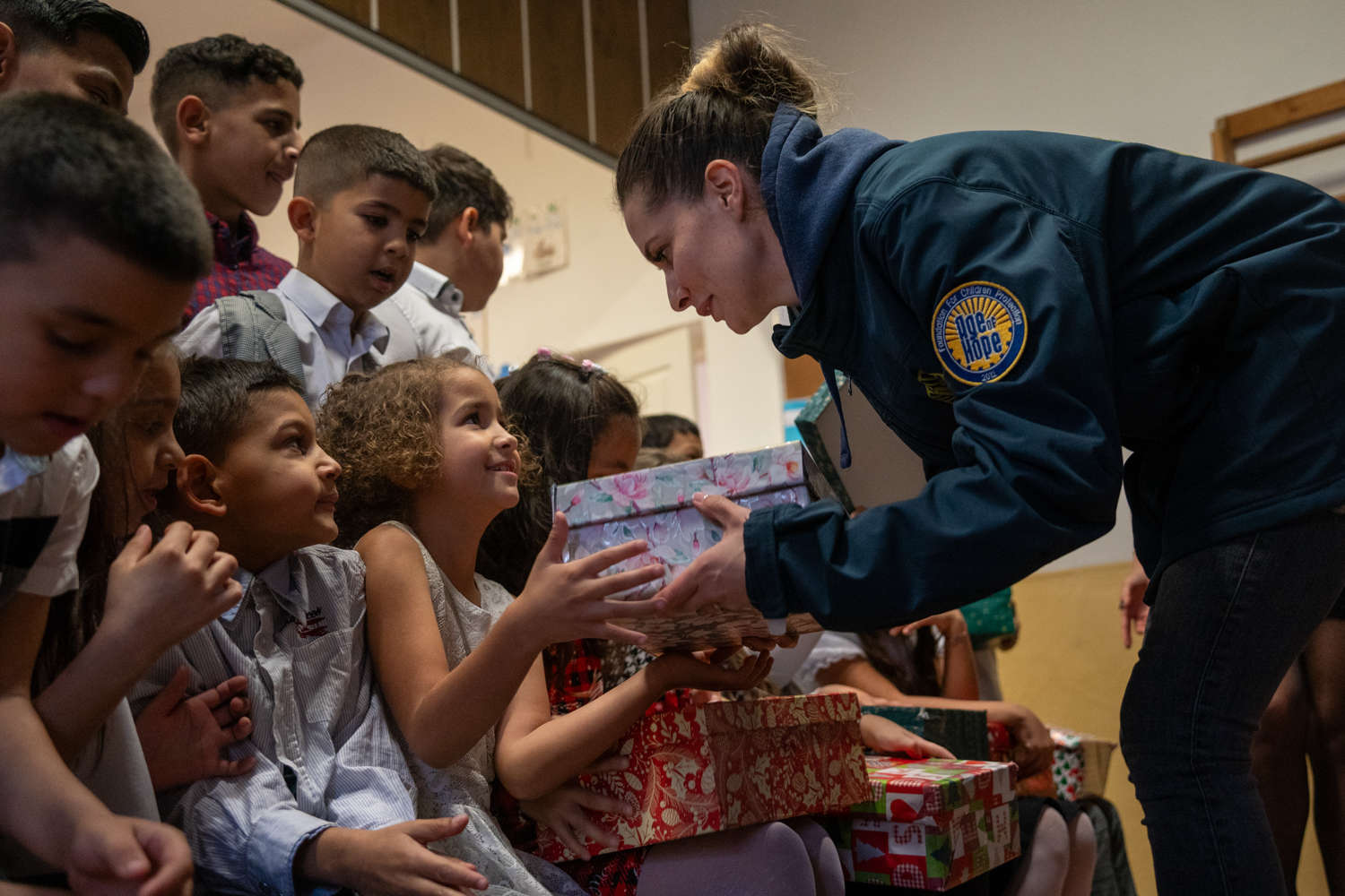 Volunteer handing out shoebox gifts to smiling children in a community hall