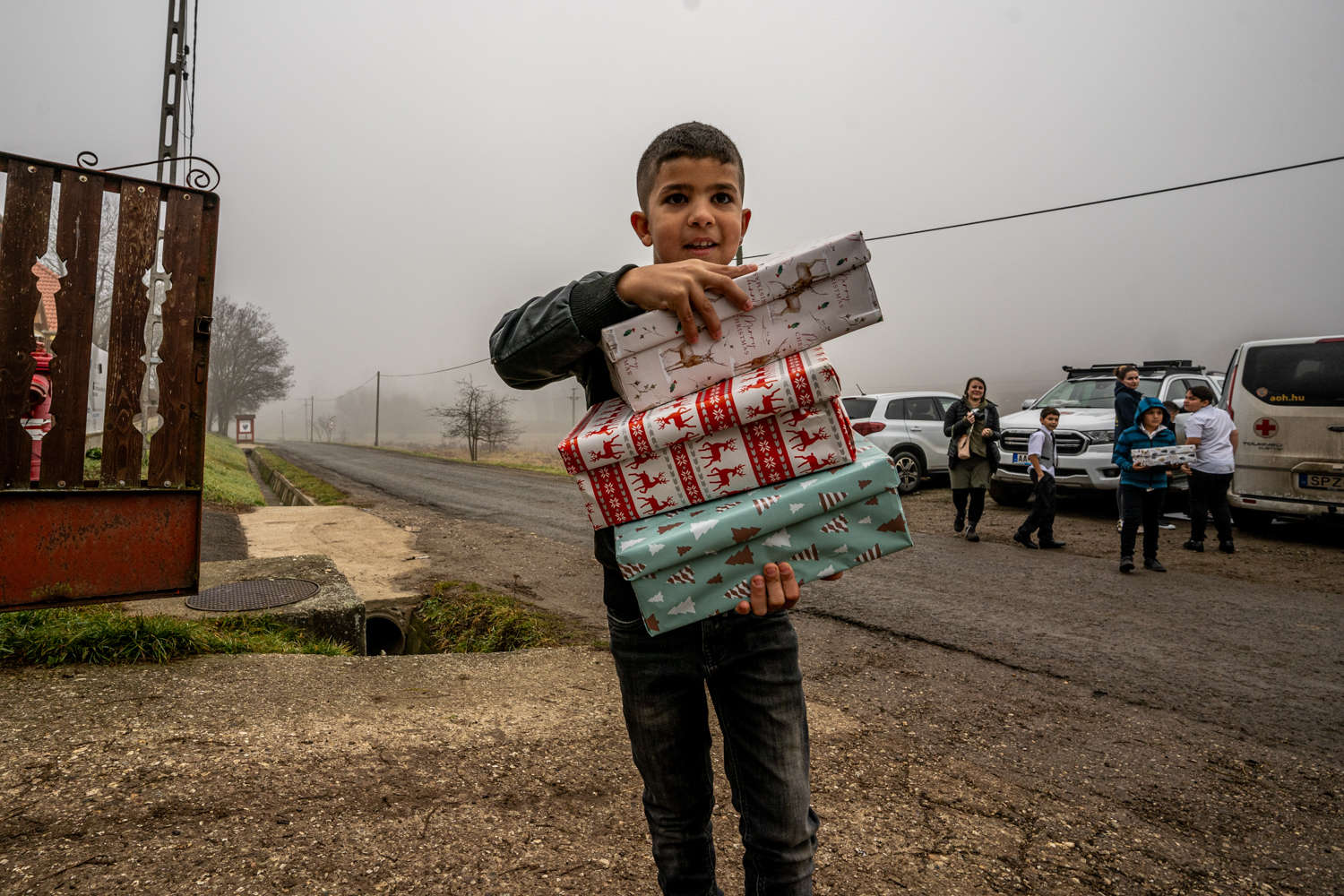 Boy proudly showing his Christmas gift packages on a foggy village road