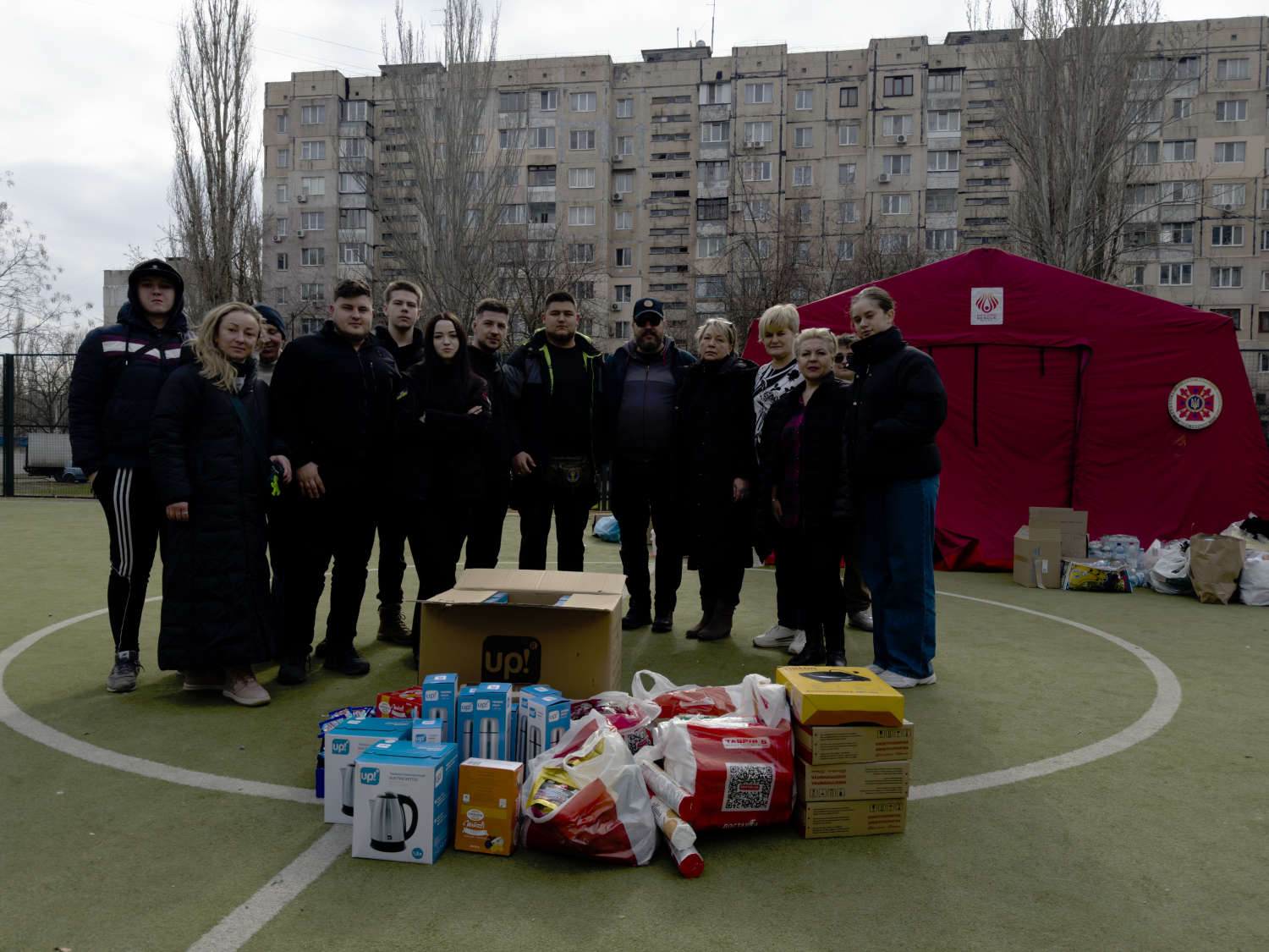 Group with aid packages on a sports field in front of a Ukrainian housing estate