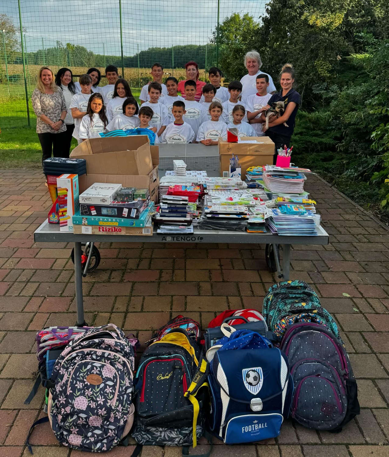 Group photo of children and volunteers during the school supplies tour, with supplies and backpacks on the table
